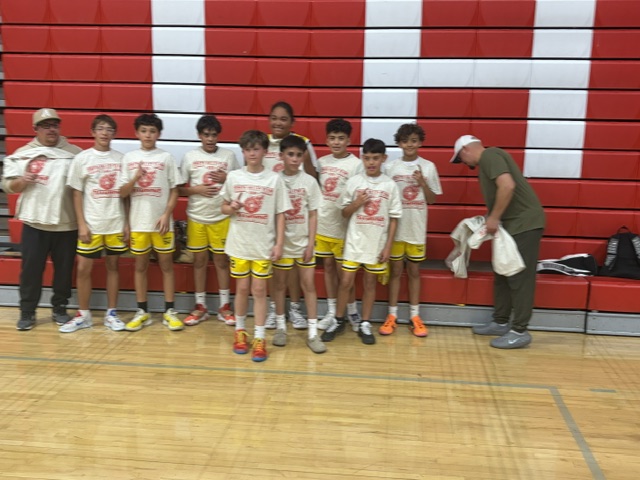Youth basketball team holding championship shirts in a gym
